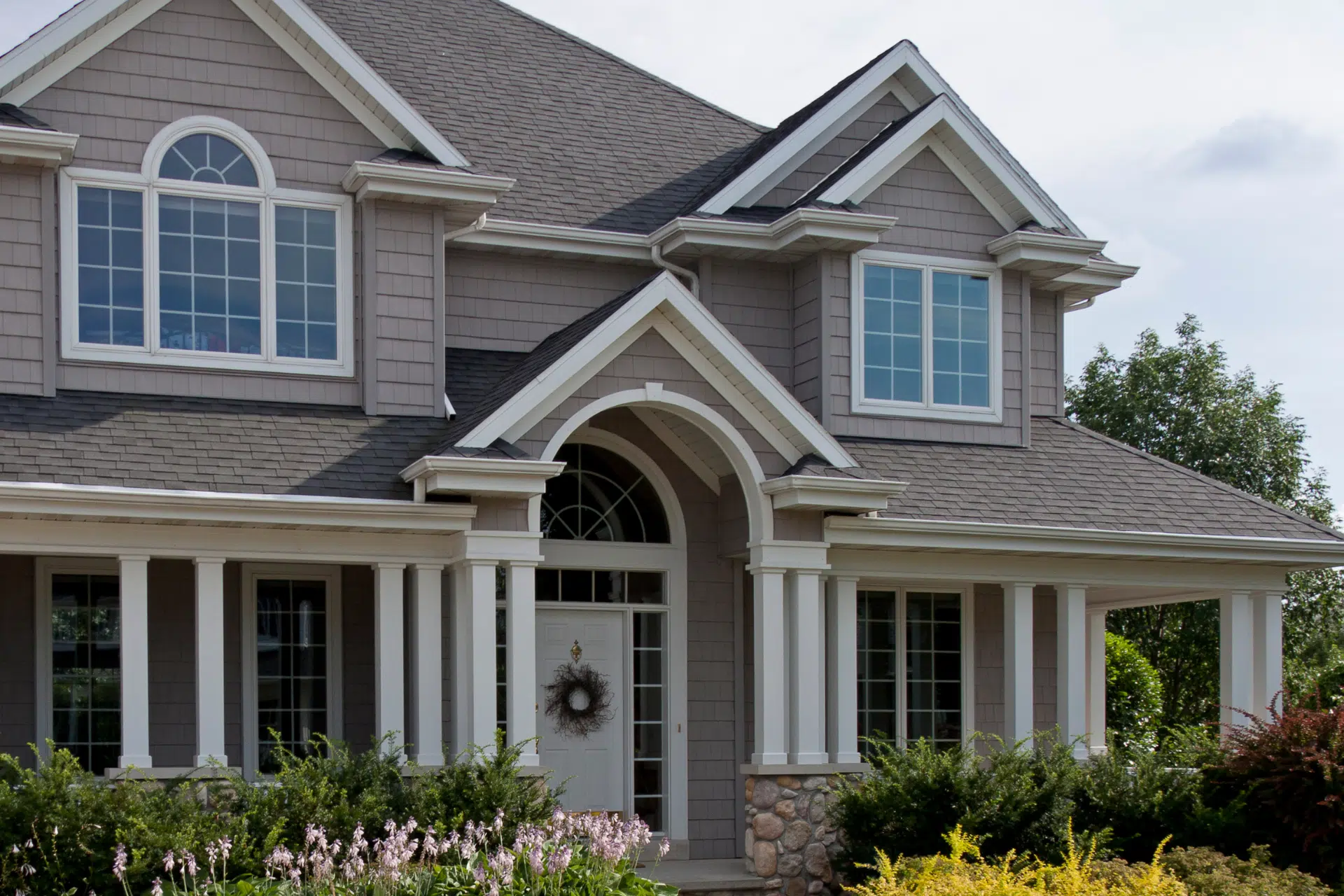 A gray house with white trim, located in Statesville NC and featuring a beautiful garden of bushes with a new roof.